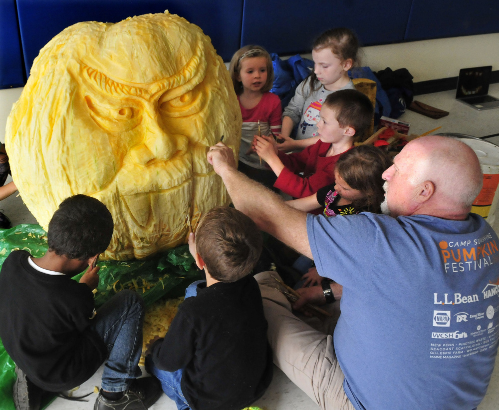Moe Auger shows kindergarten students how to use tools to carve around the face of a 400-pound pumpkin at North Elementary School in Skowhegan on Thursday.