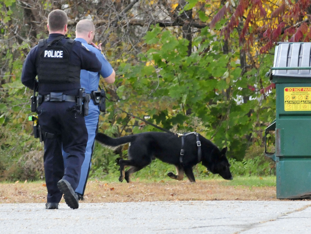 Waterville police officer Cameron Huggins, left, and a state trooper with a tracking dog search for the suspect of a burglary at the Rite Aid store on Main Street in Waterville on Thursday. The suspect, Nathan Boulette, 22, was found dead in a nearby apartment on Friday.