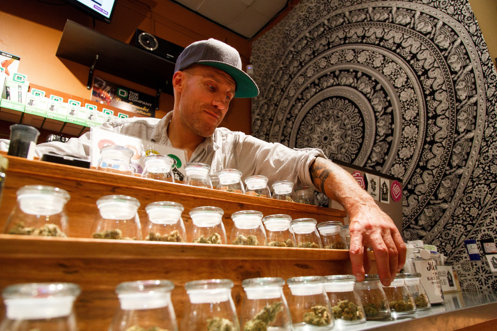 Shane Cavanaugh, owner of Amazon Organics, a pot dispensary in Eugene, Ore., arranges the cannabis display  in his store. The Associated Press