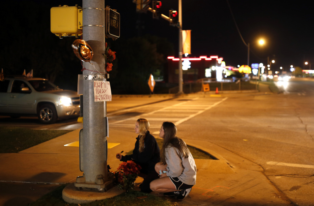 Oklahoma State students Kelly Cooke, left, and Rebecca Buchanan read messages on a memorial in Stillwater, Okla., on Saturday, near where a car crashed into spectators at the homecoming parade, killing four people.