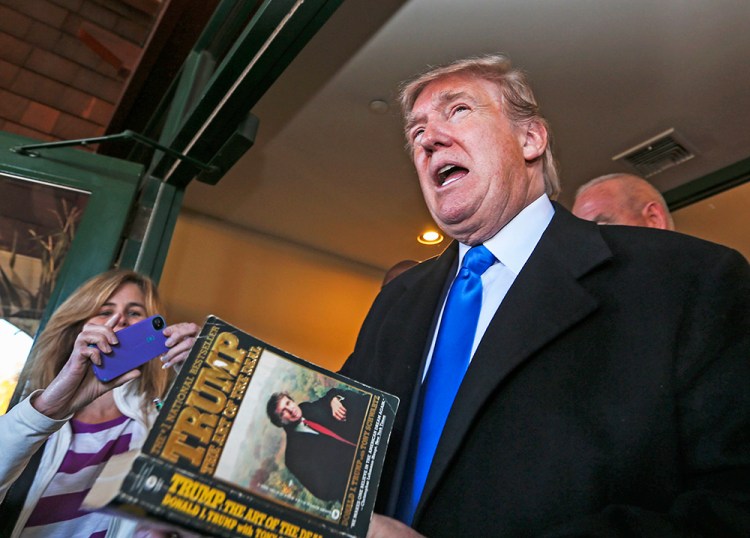 Republican presidential candidate Donald Trump autographs a book on his way out after speaking at a town hall meeting at the Atkinson Country Club in Atkinson, N.H., Monday, The Associated Press