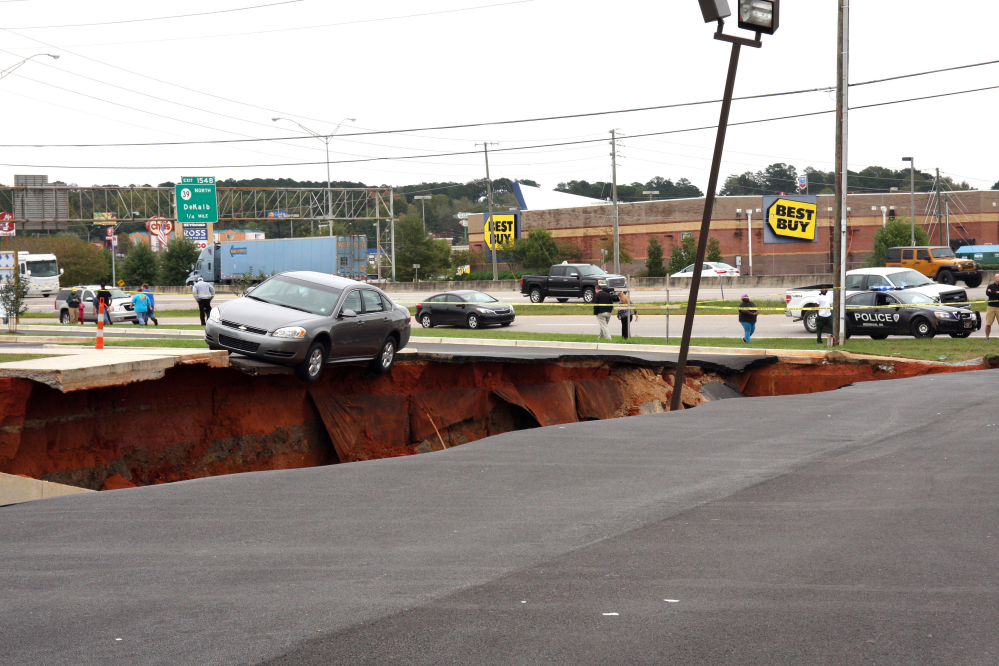 A car teeters on the edge of a cave-in of a parking lot in Meridian, Miss., Sunday.