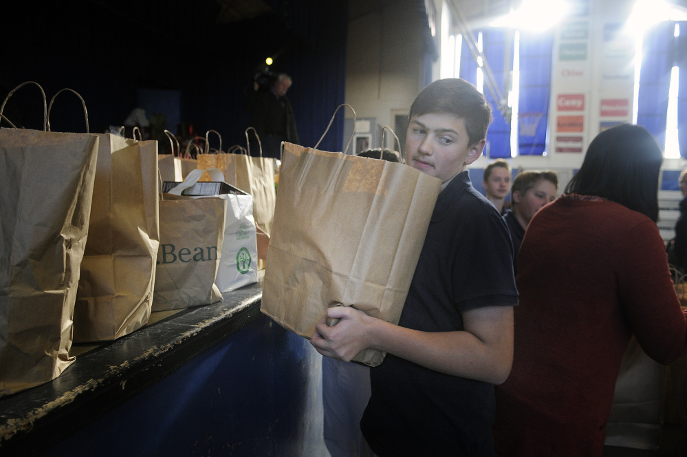 St. Michael School eight grader Drew Dionne carries a bag of Thanksgiving groceries Monday to people waiting in line at the Augusta Catholic school for food.