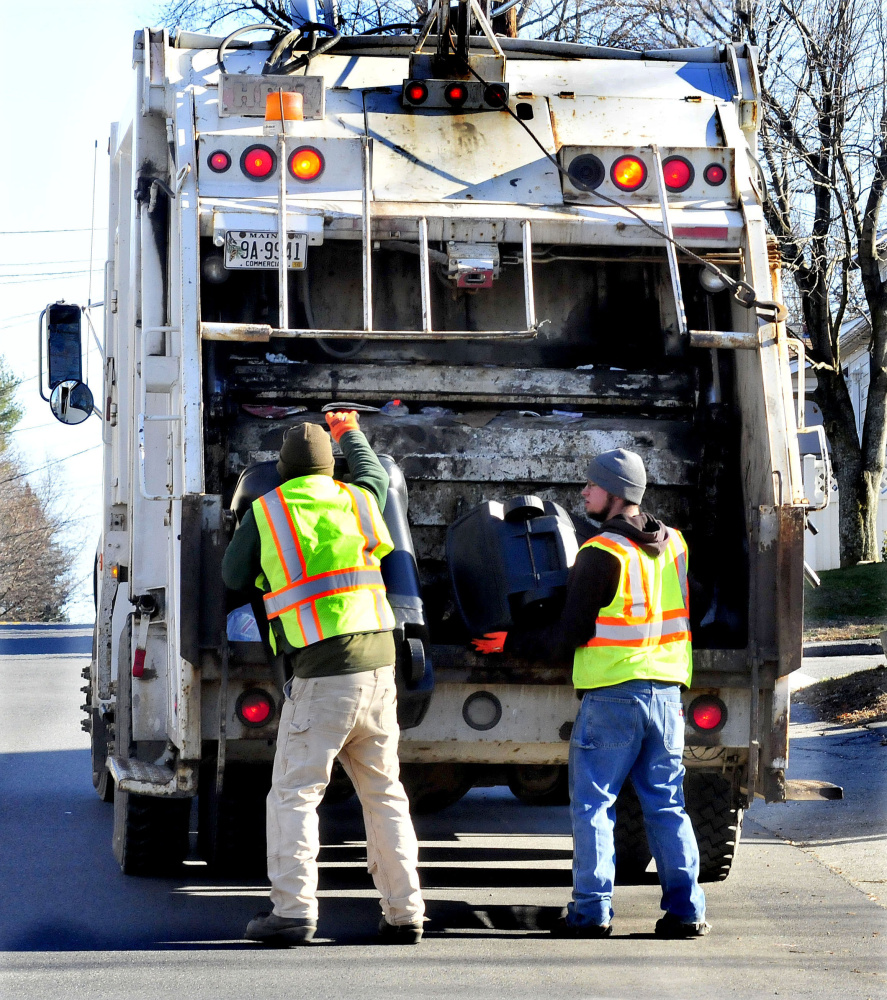 Winslow Public Works employees Josh Whitman, left, and Jacob Solomon fill a trash truck on Monday. A survey shows that Winslow residents support of more recycling in town, but are not in favor of a pay-per-bag garbage collection program.