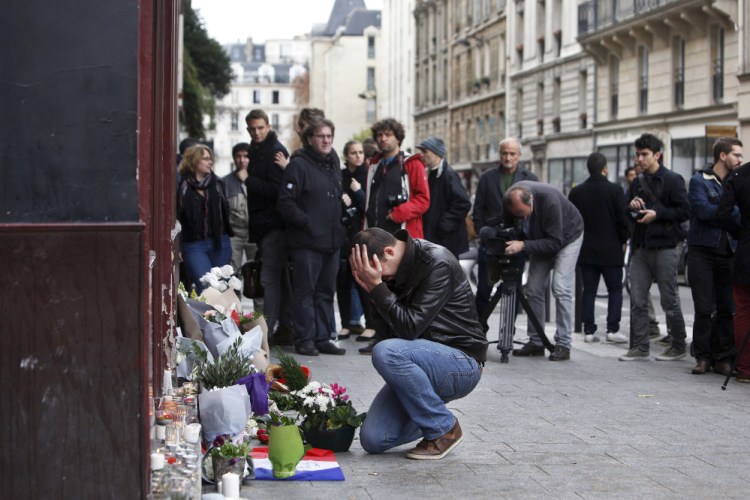 A man holds his head in his hands as he lays flowers in front of the Carillon cafe, in Paris on Saturday. French President Francois Hollande vowed to attack Islamic State without mercy as the jihadist group admitted responsibility Saturday for orchestrating the deadliest attacks inflicted on France since World War II.