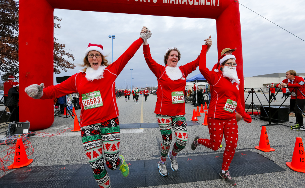 Carrie Castonguay, from left, Marjorie Fletcher and Catherine Castonguay join hands as they cross the finish line at the annual Santa Hustle Half Marathon and 5K on Sunday at the Maine Mall. The trio finished the 5K with a time of 34:49.