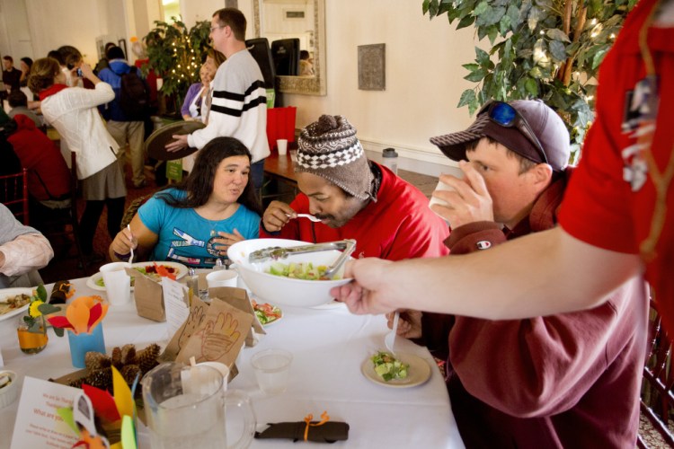 Donna Gagne, Kenny Bringle and William Dornermann, all of Portland, eat their Thanksgiving dinner as volunteer Evan Milkowski clears a bowl of salad from the table.