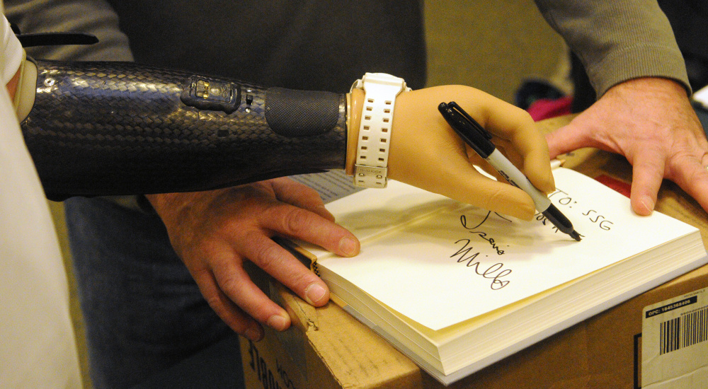 Travis Mills autographs a copy of his book “Tough As They Come” with his left prosthetic hand on Tuesday at the Barnes and Noble store in Augusta. Mills made jokes with customers that used to be right handed but had to learn to write with left.