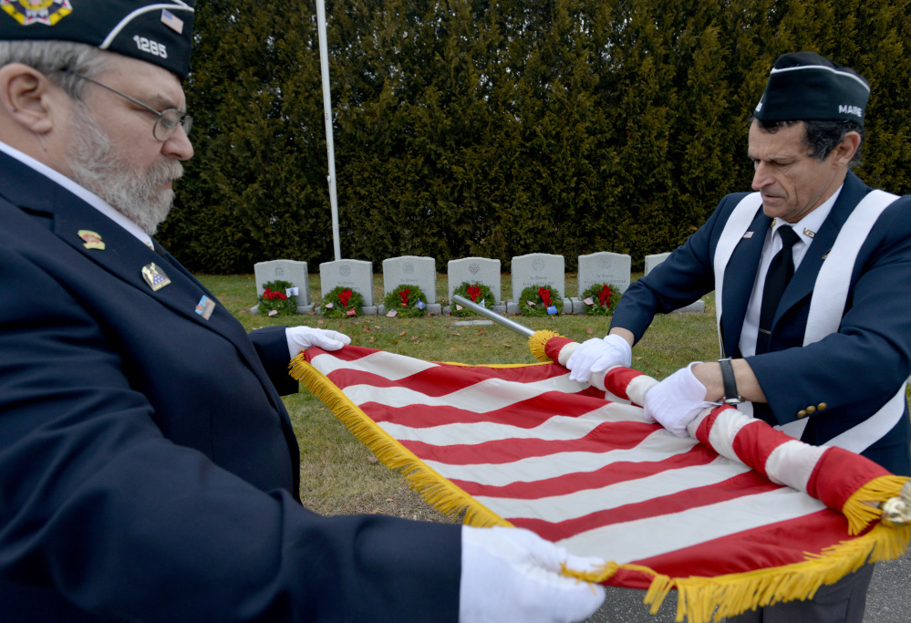 Waterville VFW post 1285 men’s auxiliary members Forrest Breton, left, and Bryant Bourgoin roll the American flag Saturday after ceremoniously placing wreaths on military veterans’ graves at St. Francis Cemetery on Grove Street in Waterville.