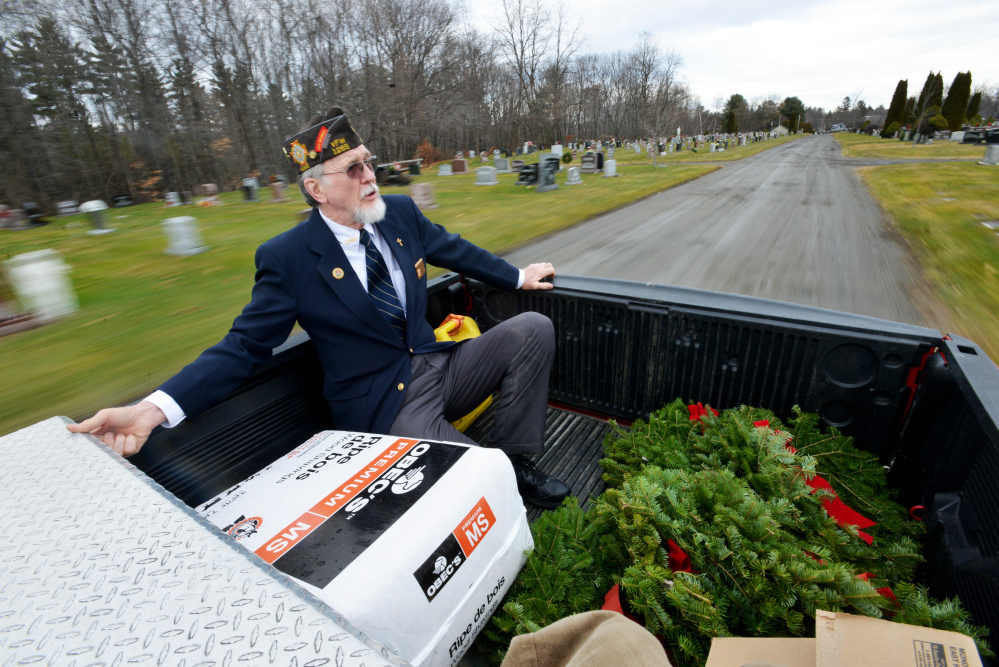 Waterville VFW Post 1285 member Charles McGillicuddy rides in the back of post Commander Daniel Parker’s pickup truck Saturday as they work their way around St. Francis Cemetery on Grove Street in Waterville to deliver wreaths to veterans’ graves.