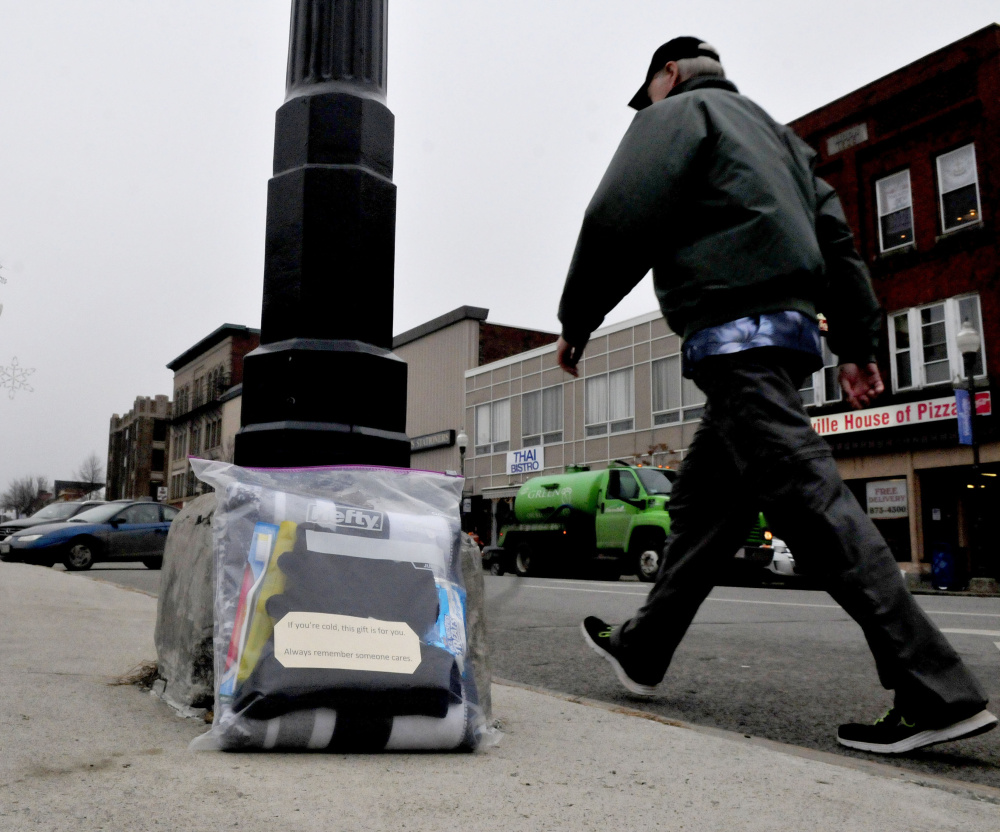 A pedestrian walks past a care package containing a blanket, snacks and toiletries on Main Street in Waterville on Monday.  The note on package says, “If you are cold this gift is for you. Always remember that someone cares.”
