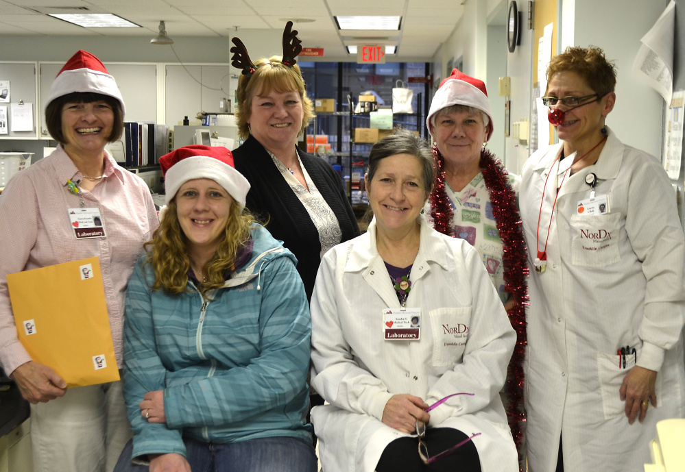 Fawn Paradis, standing, left, hands over proceeds to Shannon Mitchell, seated, left, Western Maine Community Action’s Operation Santa Claus coordinator. Seated beside Mitchell is Sandra Swatsky. Standing beside Paradis, from left, are Lesa Thompkins, Deb Sealey and Lizette Cihak.