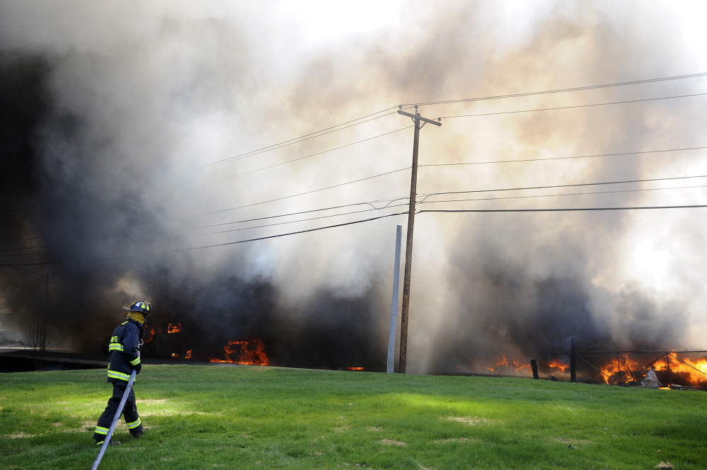 A firefighter drags a hose to an explosion May 5 while attempting to fight the blaze that destroyed AD Electric on South Monmouth Road in Monmouth.