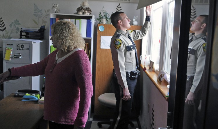 Deputy Aaron Moody and principal Christine Lajoie-Cameron examine a window Monday that a thief broke to gain entry to the Carrie Ricker School in Litchfield.