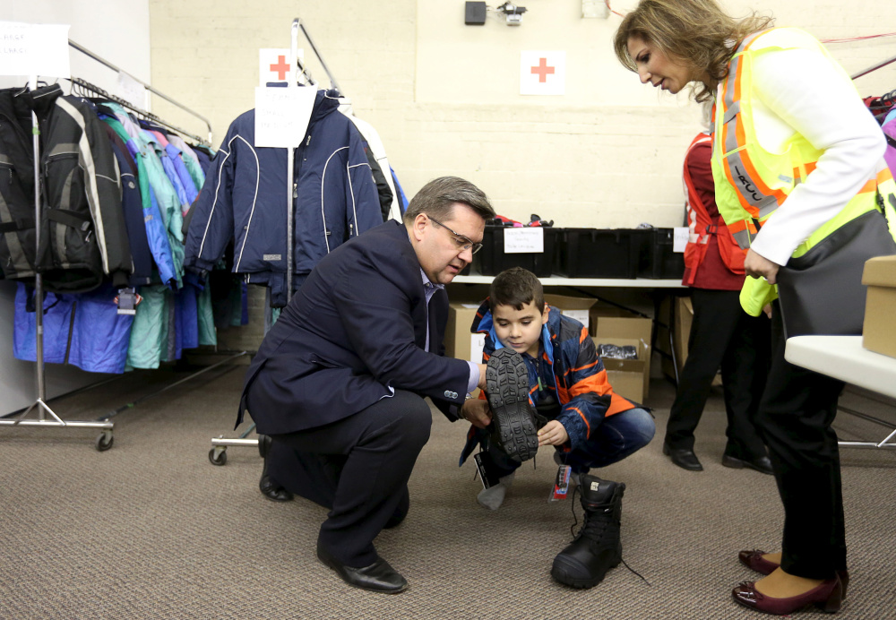 Montreal Mayor Denis Coderre helps Syrian boy Raffi Der Kaspar, 10, try on boots at the Welcome Centre in Montreal after a second military airlift of refugees arrived Saturday. Canada expects to resettle 10,000 refugees by year’s end.