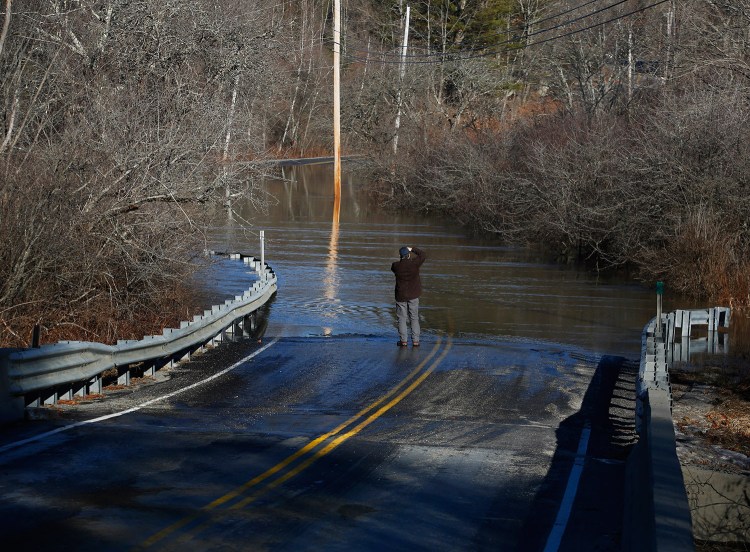 North Yarmouth resident Mike Estes takes pictures of a submerged section of West Pownal Road on Monday following a rainstorm that knocked out power to over 50,000 Maine homes.