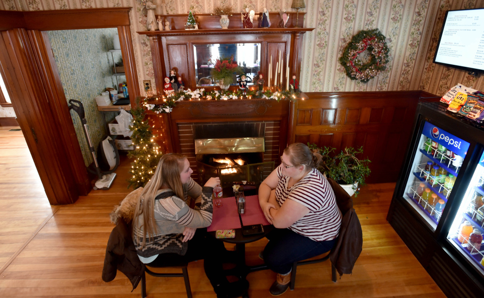 Erika Parker, left, and Anna Lorette, right, sip on coffee as they warm by the fire at M&M’s Ice Cream Parlor and Fireside cafe on Main Street in Madison on Thursday.