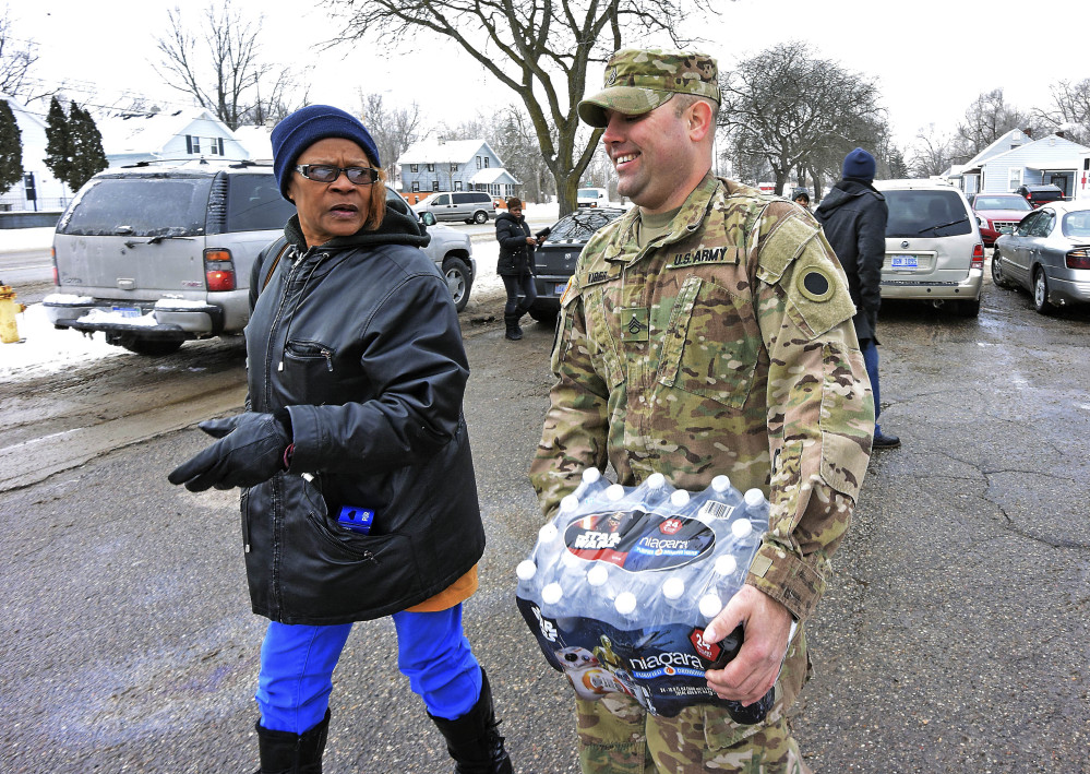 Michigan National Guard Sgt. Steve Kiger of Harrison, Mich., carries water for a resident, Wednesday Jan 13, 2016 in Flint, Mich. Members of the Michigan National Guard began arriving in Flint on Wednesday for briefings on the drinking water crisis, ahead of a larger contingent of Guardsmen who will help distribute bottled water, filters and other supplies to residents. (Dale G. Young/Detroit News via AP)  DETROIT FREE PRESS OUT; HUFFINGTON POST OUT; MANDATORY CREDIT
