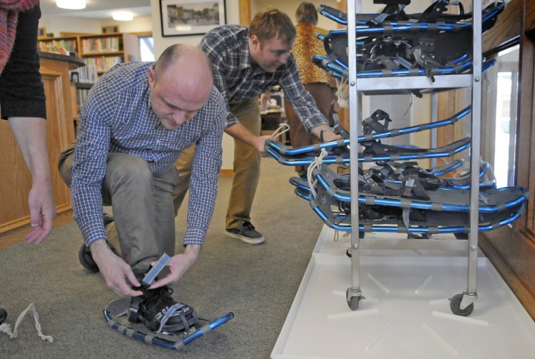 Bailey Library Director Richard Fortin, right, stacks snowshoes Wednesday as Adult Services Librarian Shane Billings learns how to lace a pair from volunteer Margy Burns Knight in Winthrop. The snowshoes, purchased through a donation, are available for check out.