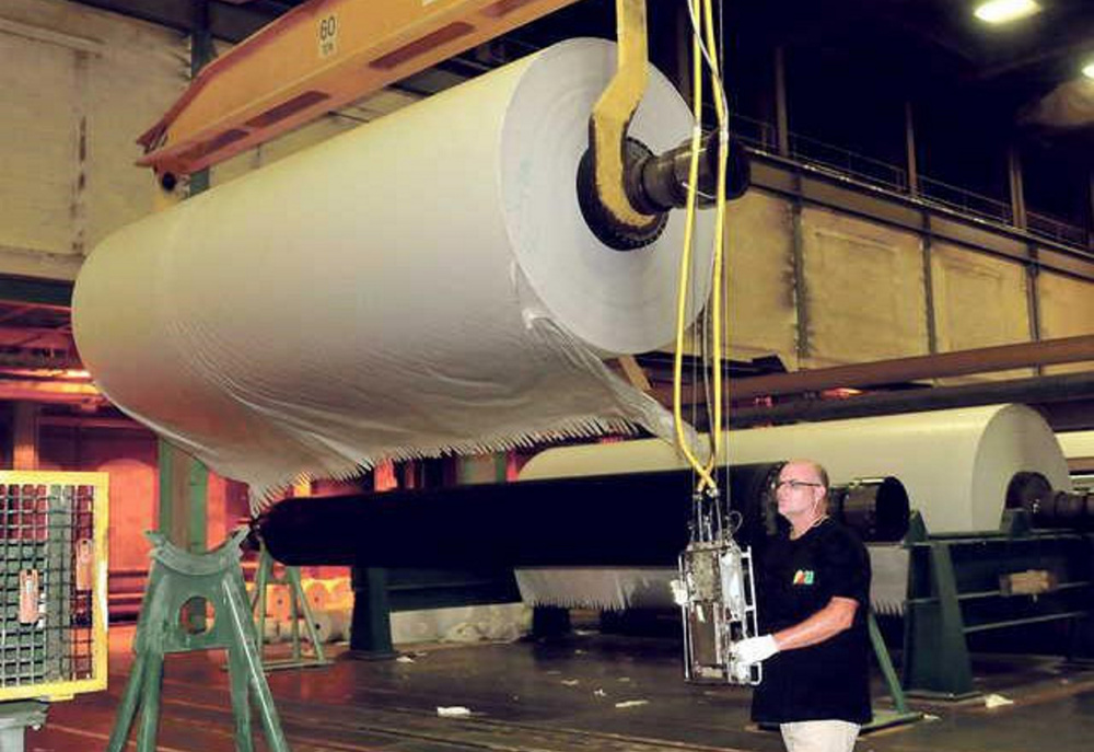 A worker at Madison Paper Industries handles a roll of paper in August. The mill has cut back production to five days a week from seven, meaning a cut in wages for workers, their union says. The cuback could last as long as sic months.