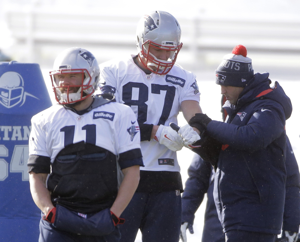 Patriots tight end Rob Gronkowski, center, has his arm tended to as wide receiver Julian Edelman, left, warms up at practice on Wednesday. Gronkowski did not practice on Thursday because of knee and back injuries, but the team reportedly believes he will play Saturday against the Chiefs.
