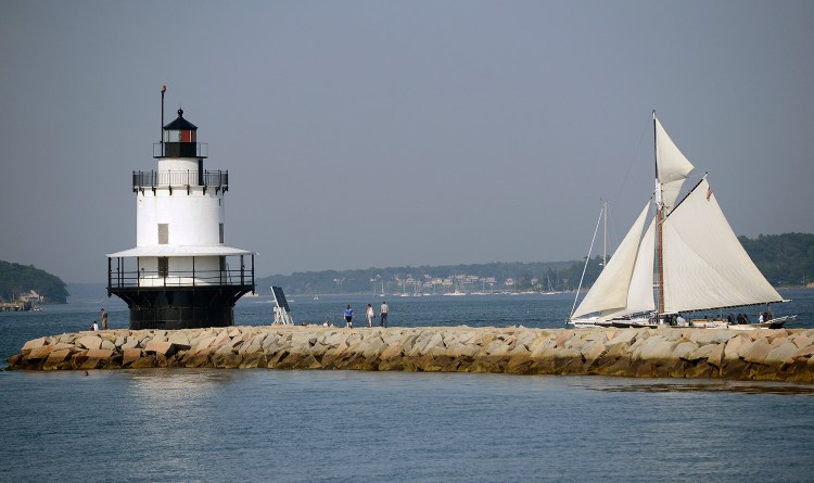A sailboat navigates past Spring Point Ledge Lighthouse as visitors walk out on the breakwater in South Portland.