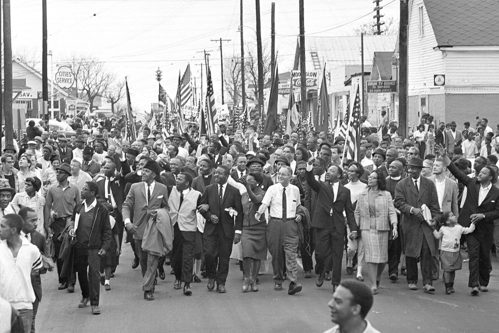 Martin Luther King, just right of center, waves to onlookers as he leads marchers across a bridge over the Alabama River on the first of a five-day, 50-mile march to the state capitol at Montgomery on March 21, 1965.