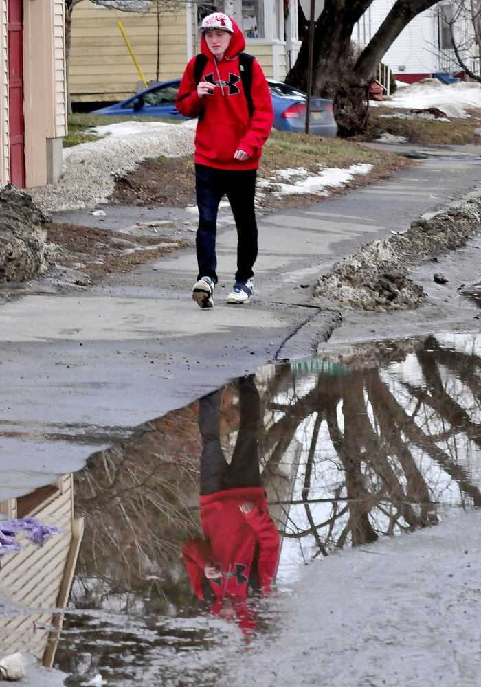 Noah Burnham is reflected in water that is usually frozen this time of year while walking in Waterville on Monday. Asked his opinion on the recent warm temperatures Burnham said, “I like it a lot.”