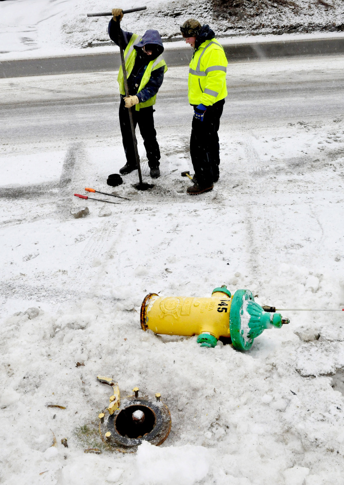 Ryan Adams, left, and Tony Bellavance, of the Kennebec Water District, repair a fire hydrant that was knocked over by a driver whose vehicle slid off North Street as snow covered the road on Wednesday. Adams said the hydrants are designed to break away and limit damage. 