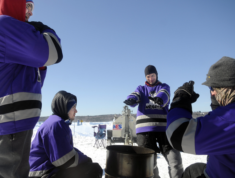 The Mad Hatters, of Portland, warm up Sunday in front of a fire during the Maine Pond Hockey Classic at the Snow Pond Center for the Arts in Sidney.