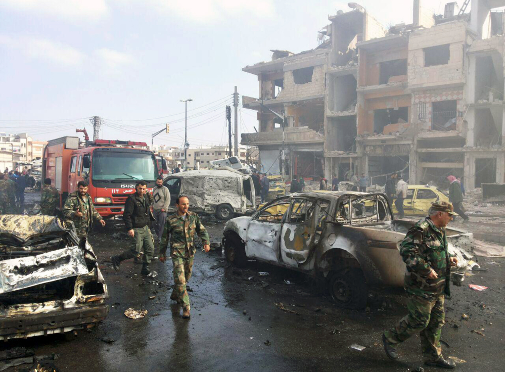 In this photo released by the Syrian official news agency SANA, Syrian citizens gather at the scene where two blasts exploded in the pro-government neighborhood of Zahraa, in Homs province, Syria, Sunday.