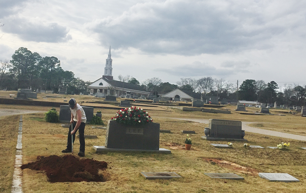 A man rakes dirt over a grave in the Lee family cemetery plot, Saturday in Monroeville, Ala.