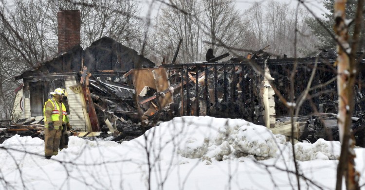 Firefighters outside the burned remains of a home on the Pease Hill Road in Anson on Wednesday. The fire is being investigated as a possible arson.