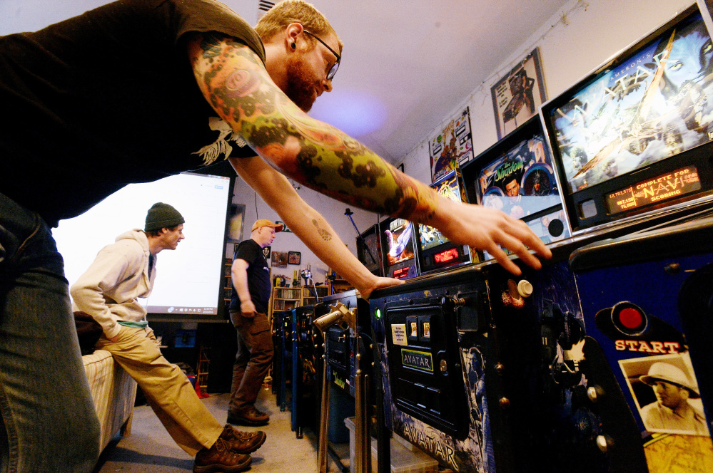 Tucker Daniels of Portland, sporting pinball tattoos, concentrates on a game of pinball as Matt Lodgek of Gorham, left, and Jerry Lindsay of Oakland take turns playing against each other during the IFPA Maine State Pinball Championship in Gorham on Saturday.