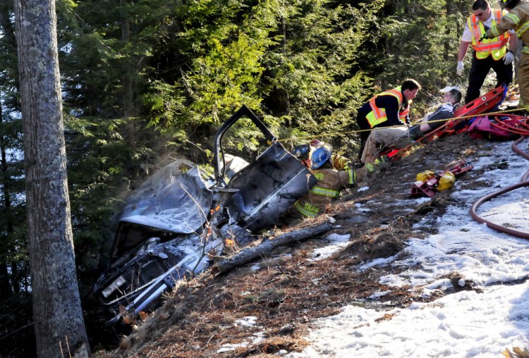 Firefighters pull an injured man strapped in a gurney up a steep embankment after he was removed from this vehicle that went off Route 135 in Belgrade on Tuesday.
