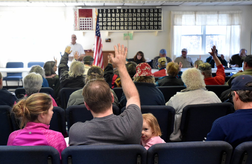 Marc Courtemanche, back left, stands at a lectern to moderate the Town Meeting as Olivia Boyd, 2, peeks from under her father’s arm during a vote Saturday at the Athens Town Office.