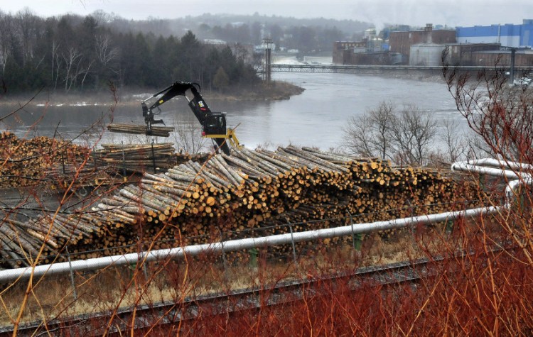 A worker unloads logs in a wood yard that will be used to make paper at the Madison Paper Industries mill in Madison, background, on Tuesday.  