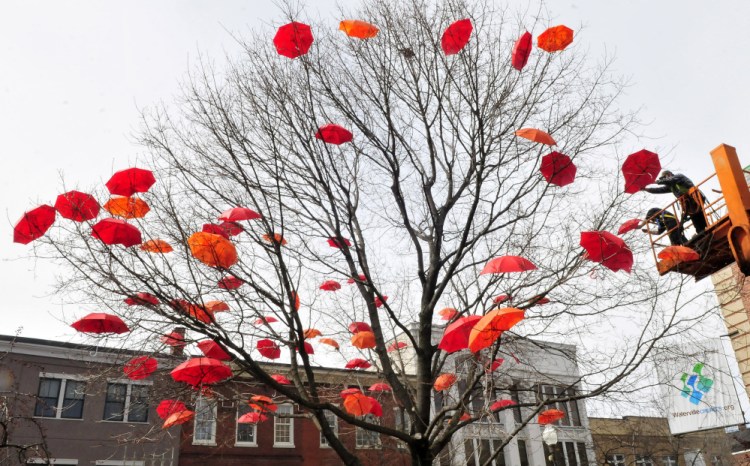 Jacob Chambers, left, and Chris Demerchant, of the Waterville Public Works Department, attach umbrellas to a tree Wednesday in Castonguay Square in Waterville. The umbrellas are part of a celebration of the visual and performing arts in the city.
