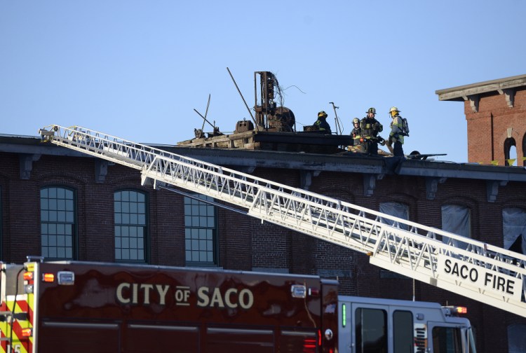 Firefighters work on the roof of Mill Building 4 on Saco Island Tuesday morning. There was fire on the roof and the second, third and fourth floors when Saco and Biddeford crews arrived on scene.
