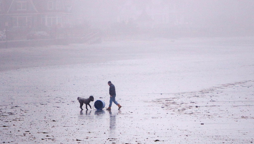 David Jones of Kennebunk rolls a bait barrel up to the sea wall at Gooch's Beach in Kennebunk while walking his dog Fritz at the beach on Friday morning. The barrel had washed ashore overnight and the high tide at midnight resulted in some splash over that created minor flooding along parts of the coast. 