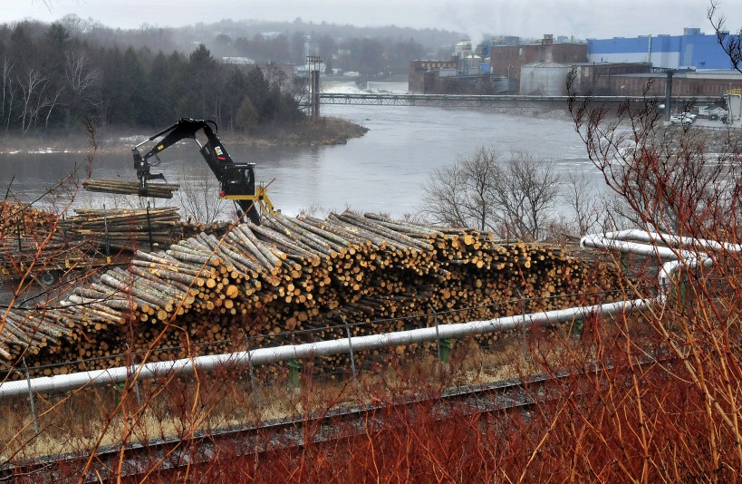 A worker unloads logs in a wood yard at the Madison Paper Industries, with the mill in the background, in March. The U.S. Department of Labor has approved funding for a program that will help retrain the more than 200 workers who will lose their jobs when the mill closes in May.