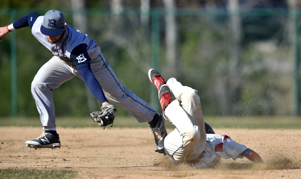 Thomas College's Tristan Pena dives safely under the tag from New England College's Tomas Pueyo (14) in the first inning of the second game of a doubleheader Saturday at Thomas College in Waterville.