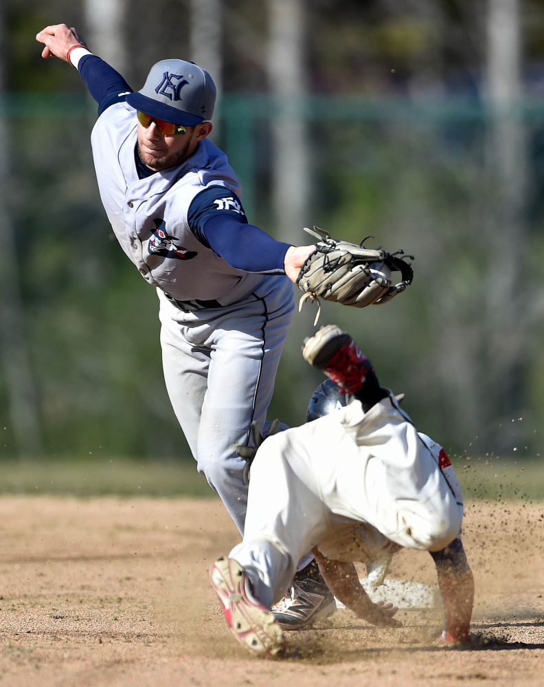 Thomas College's Tristan Pena dives safely under the tag from New England College's Tomas Pueyo (14) in the first inning of the second game of a doubleheader Saturday at Thomas College in Waterville.