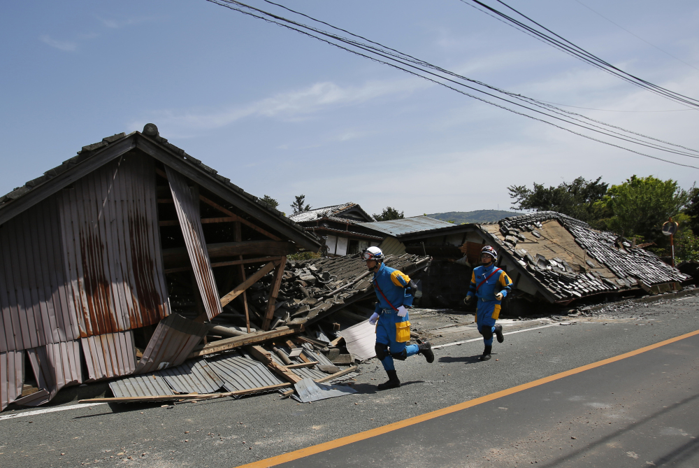 Police officers run in front of collapsed houses in Mashiki, Kumamoto prefecture, southern Japan, on Friday after the first earthquake struck.