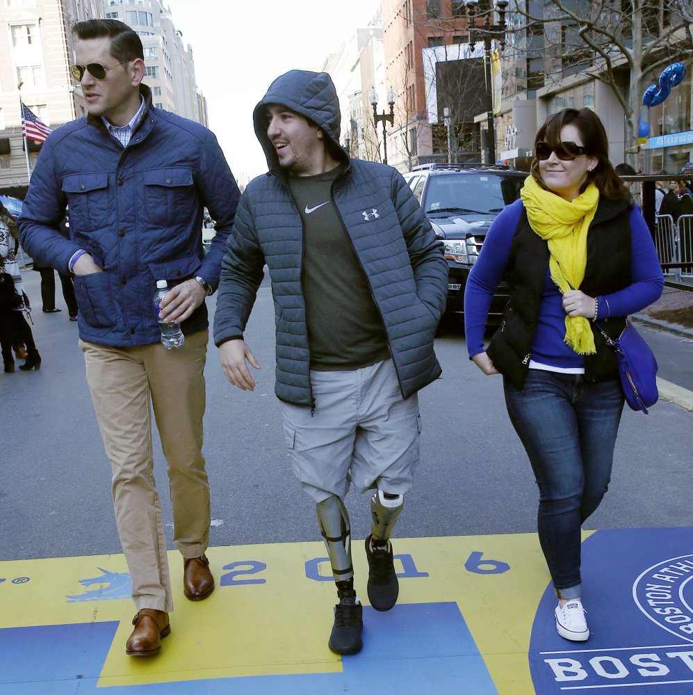 Boston Marathon bombing survivor Jeff Bauman, center, walks across the race's finish line Friday. He was among more than 260 injured in the 2013 bombings.