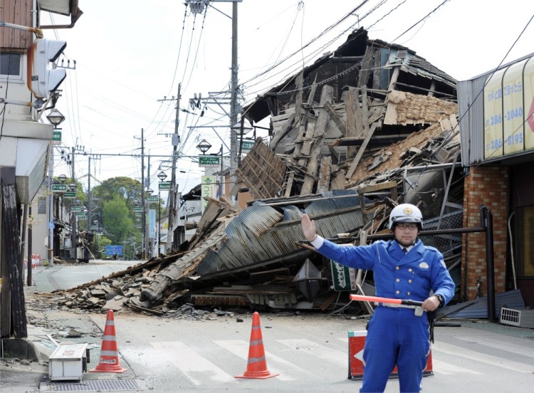 A police officer stands guard in front of a house destroyed by an earthquake in Mashiki, Kumamoto prefecture, southern Japan Saturday.