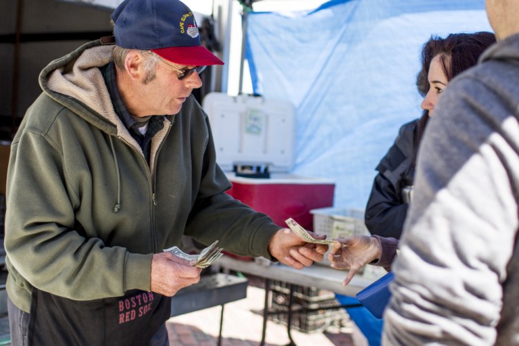  Jodie Jordan of Alewive's Brook Farm receives cash for a transaction from Candy Arno of Windham on a chilly Wednesday, one week before the market officially opens. Gabe Souza/Staff Photographer