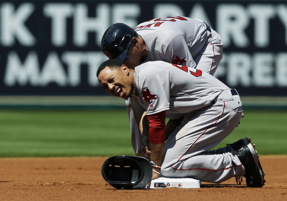 Boston Red Sox's Mookie Betts grimaces as first base coach Ruben Amaro Jr checks on him after he was hit by an errant throw from Houston Astros pitcher Mike Fiers on a pickoff attempt at first base during the first inning of a baseball game Saturday, April 23, 2016, in Houston. (AP Photo/Pat Sullivan)