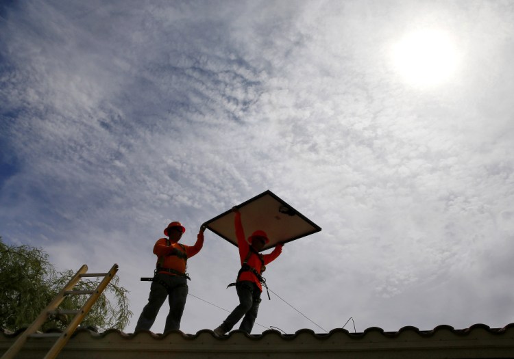 In this July 28, 2015, photo, electricians Adam Hall, right, and Steven Gabert, install solar panels on a roof for Arizona Public Service company in Goodyear, Ariz. Thanks to falling prices, investment in solar and wind power projects has outpaced investment in fossil-fueled power plants for the second straight year, according to the U.S. Department of Energy.