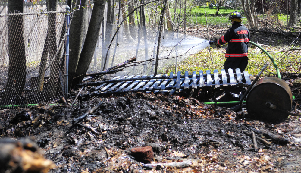 Gardiner firefighter Roy Girard sprays down the area burned by a small brush fire Tuesday behind homes on Pleasant Street in Gardiner.